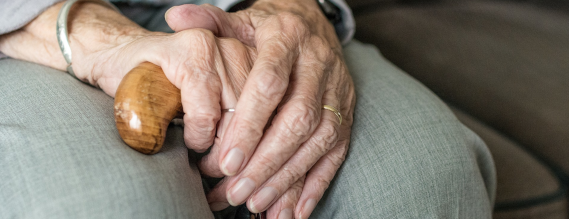 Nærbillede af en siddende ældre persons to hænder, som holder en stok 